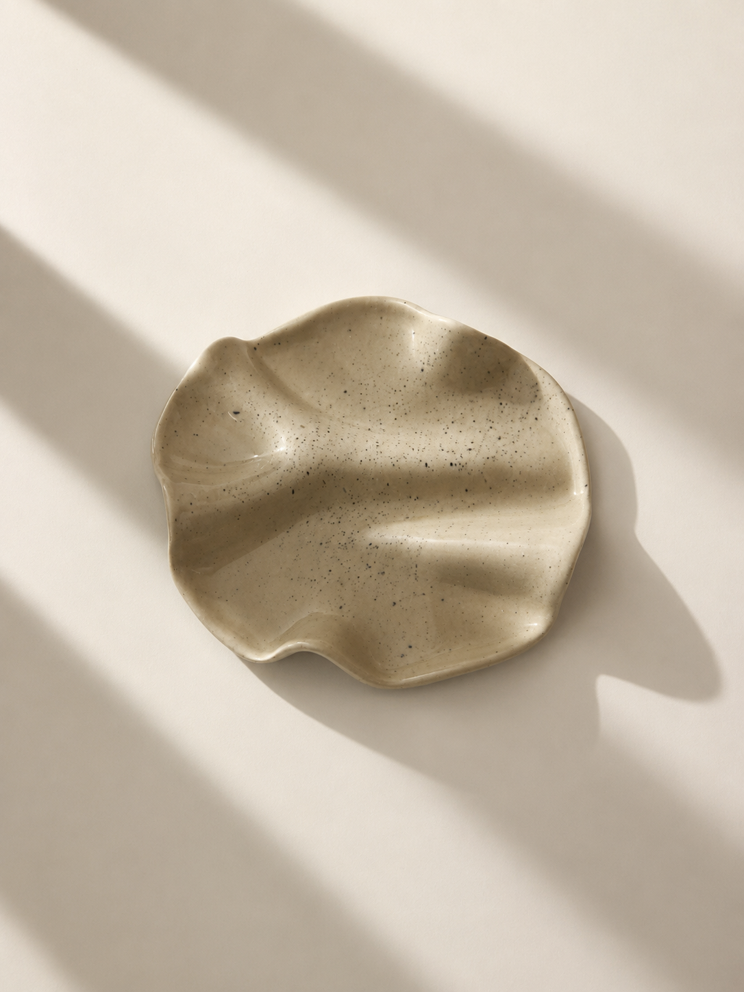 Top-down view of speckled ivory ceramic plate with organic ruffled edge on grey background