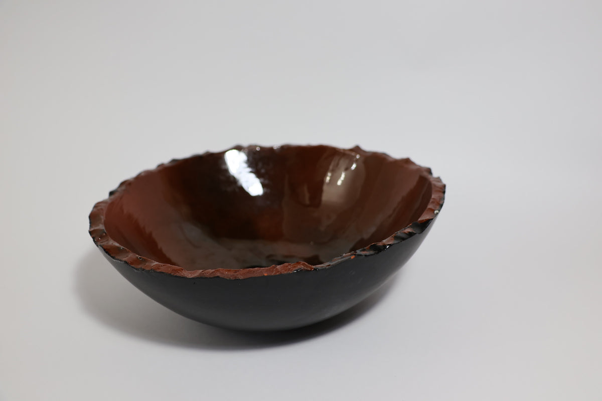 Earth-tone ceramic bowl with black exterior and amber gold glazed interior, raw edge rim