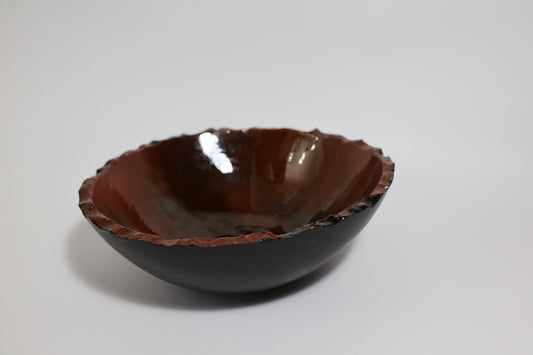 Earth-tone ceramic bowl with black exterior and amber gold glazed interior, raw edge rim
