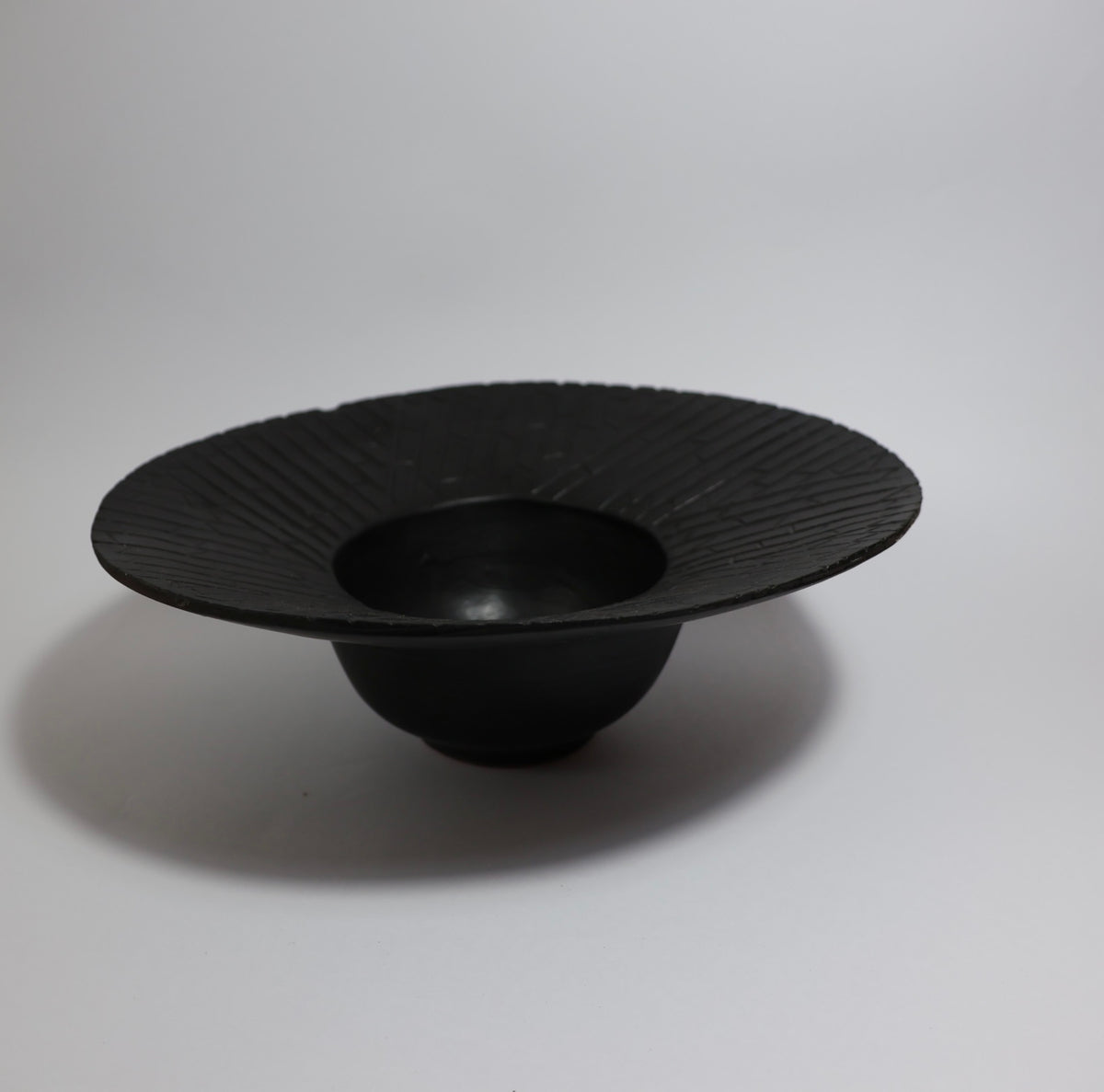 Matte black wide-rim ceramic bowl side view showing deep centre well and pedestal base