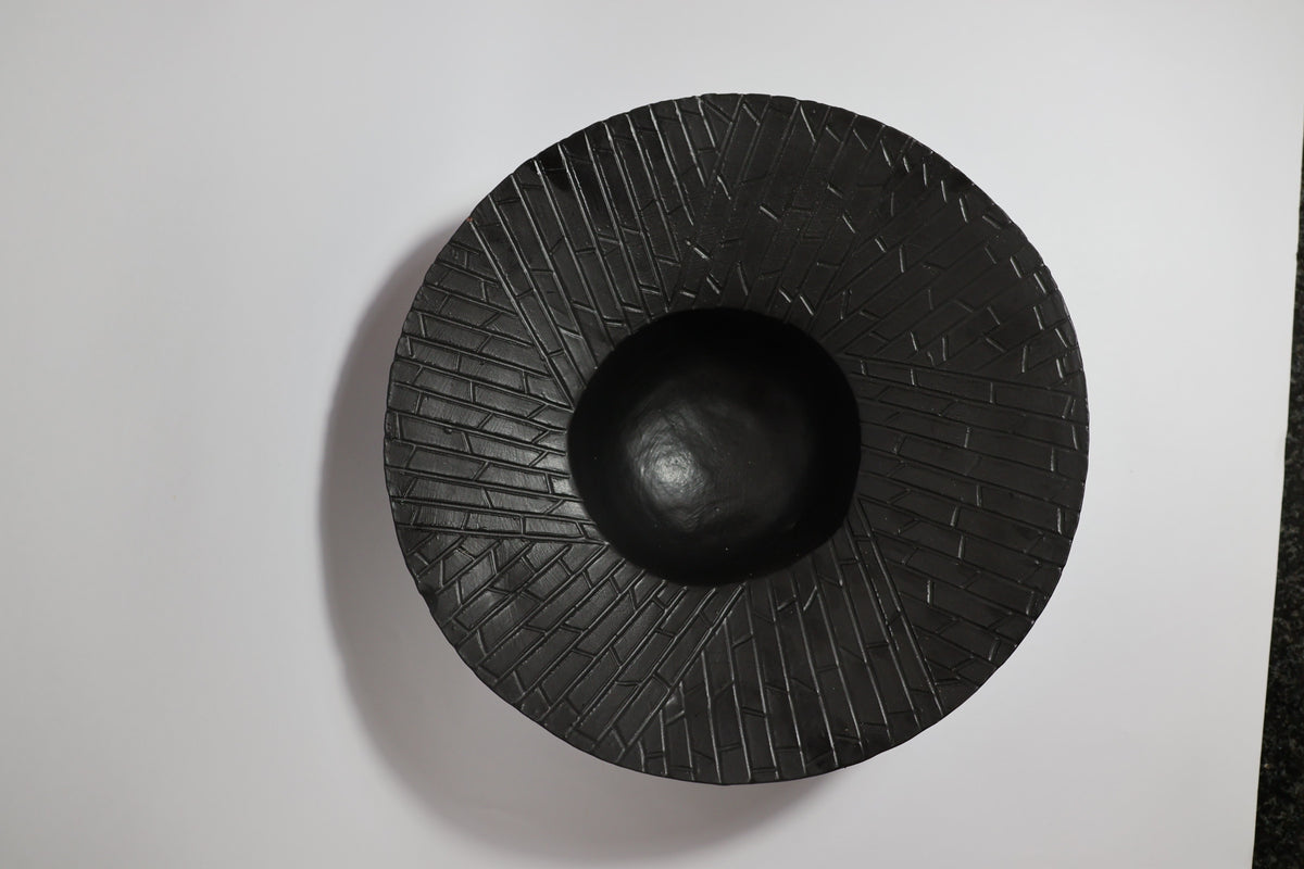 Top-down view of black ceramic bowl showing hand-carved linear texture on wide rim